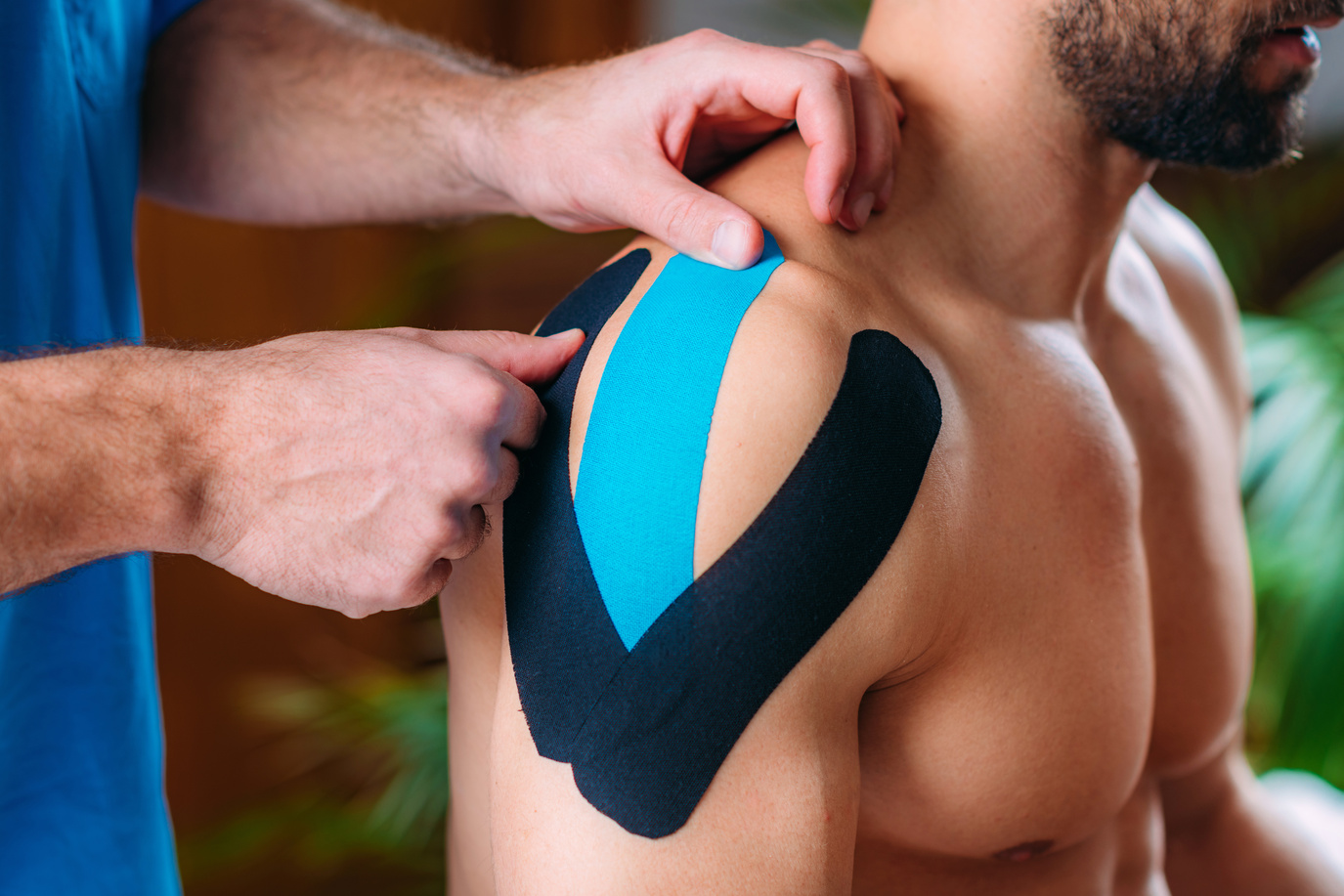 Therapist Taping Man’s Shoulder with Elastic Therapeutic Kinesiology Tape